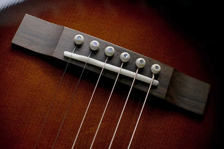 closeup of an acoustic guitar bridge and bridge pins