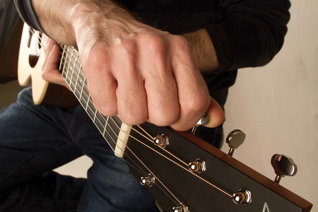 close up of a hand tuning an acoustic guitar